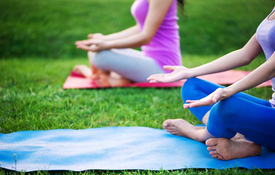 Vista de dos mujeres que tienen su sesión de yoga en un campo de hierba
