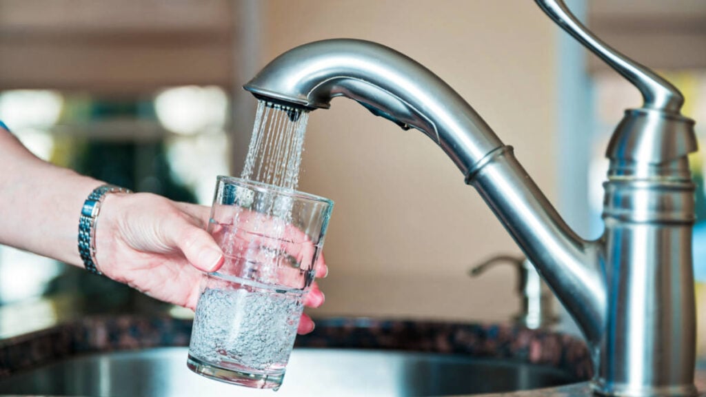 Una mano llenando el vaso con agua del grifo.