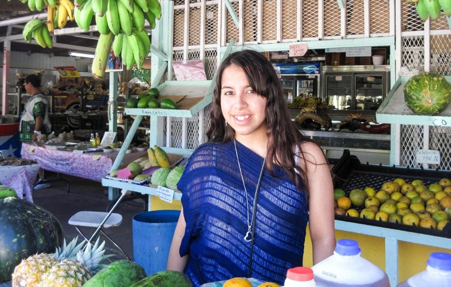 La autora con frutas a su alrededor en el Mercado de Puerto Rico