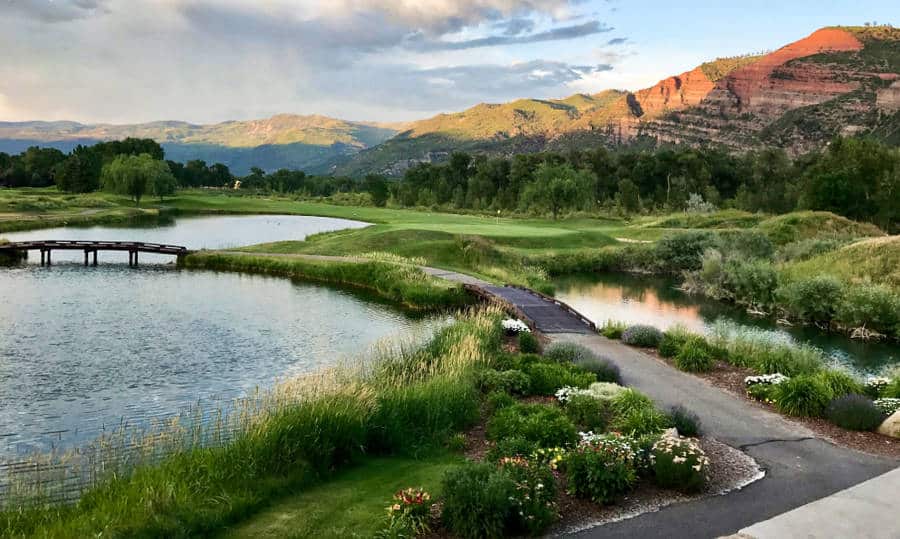 Puesta de sol sobre un campo de golf cerca del lago con acantilados de roca roja en el fondo